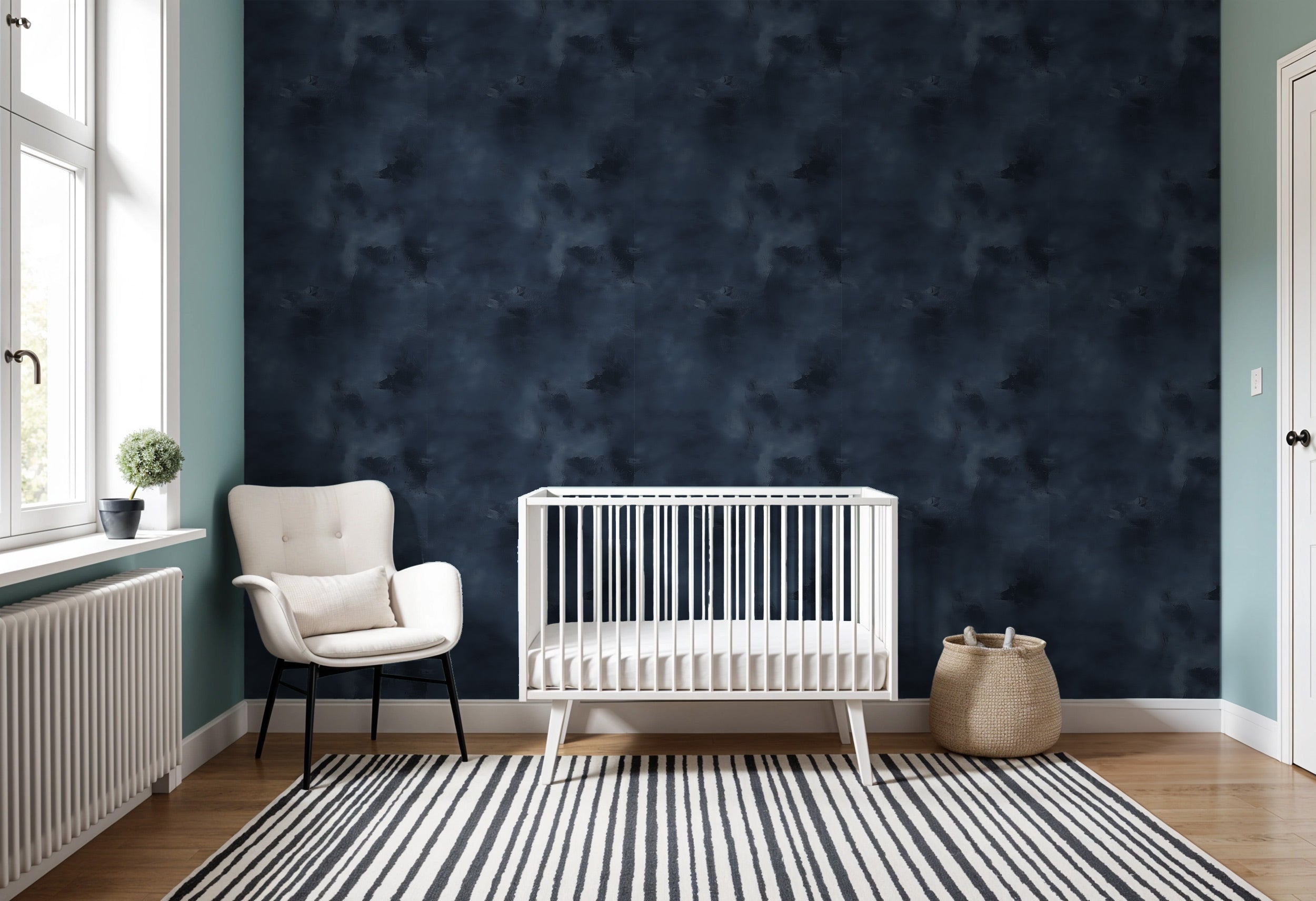 Navy blue abstract textured wallpaper in a nursery with white crib, cream chair, and striped rug for a calm transitional spac
