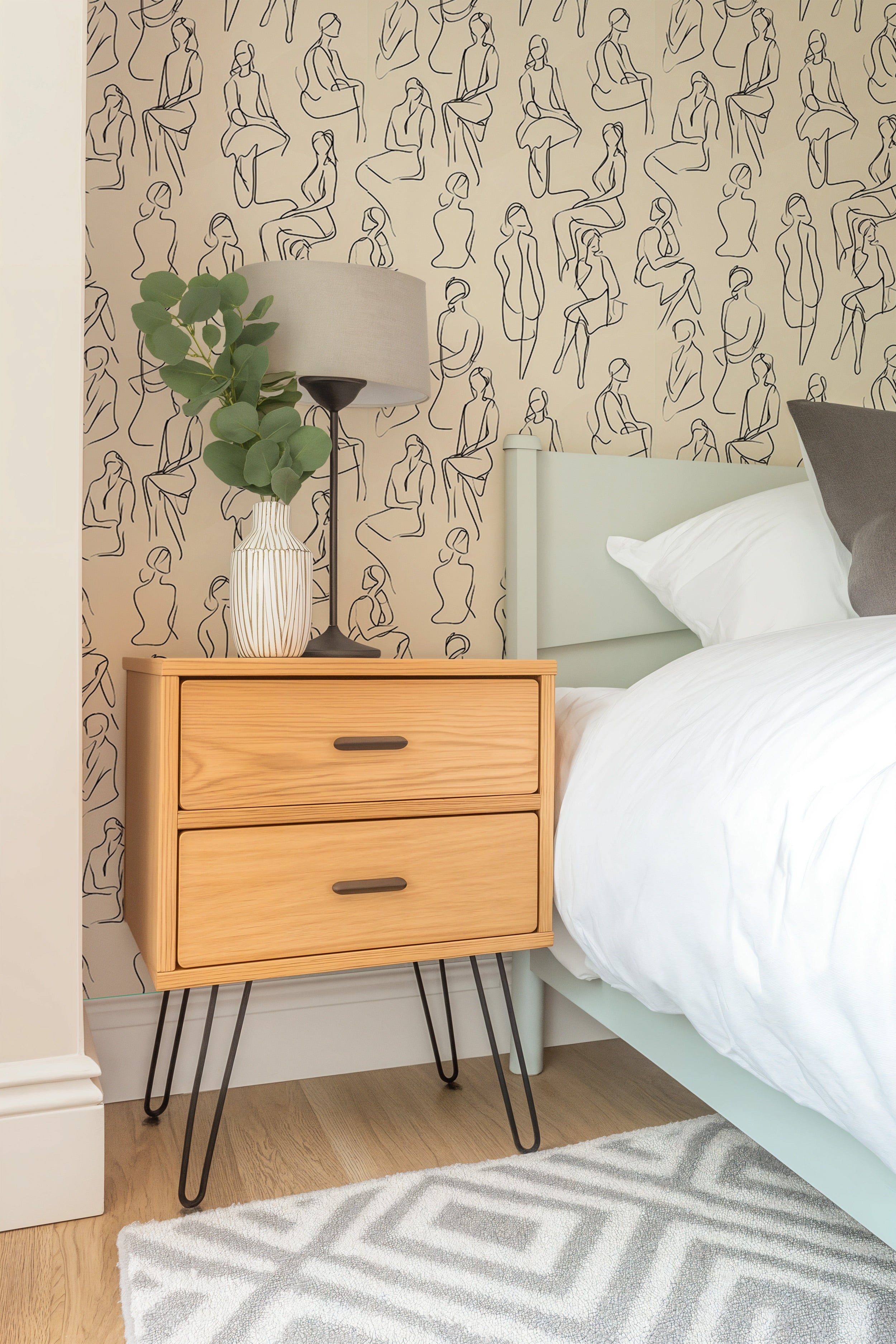 Beige minimalist wallpaper with black line art figures beside a light wood nightstand and bed in a modern bedroom, soft neutr