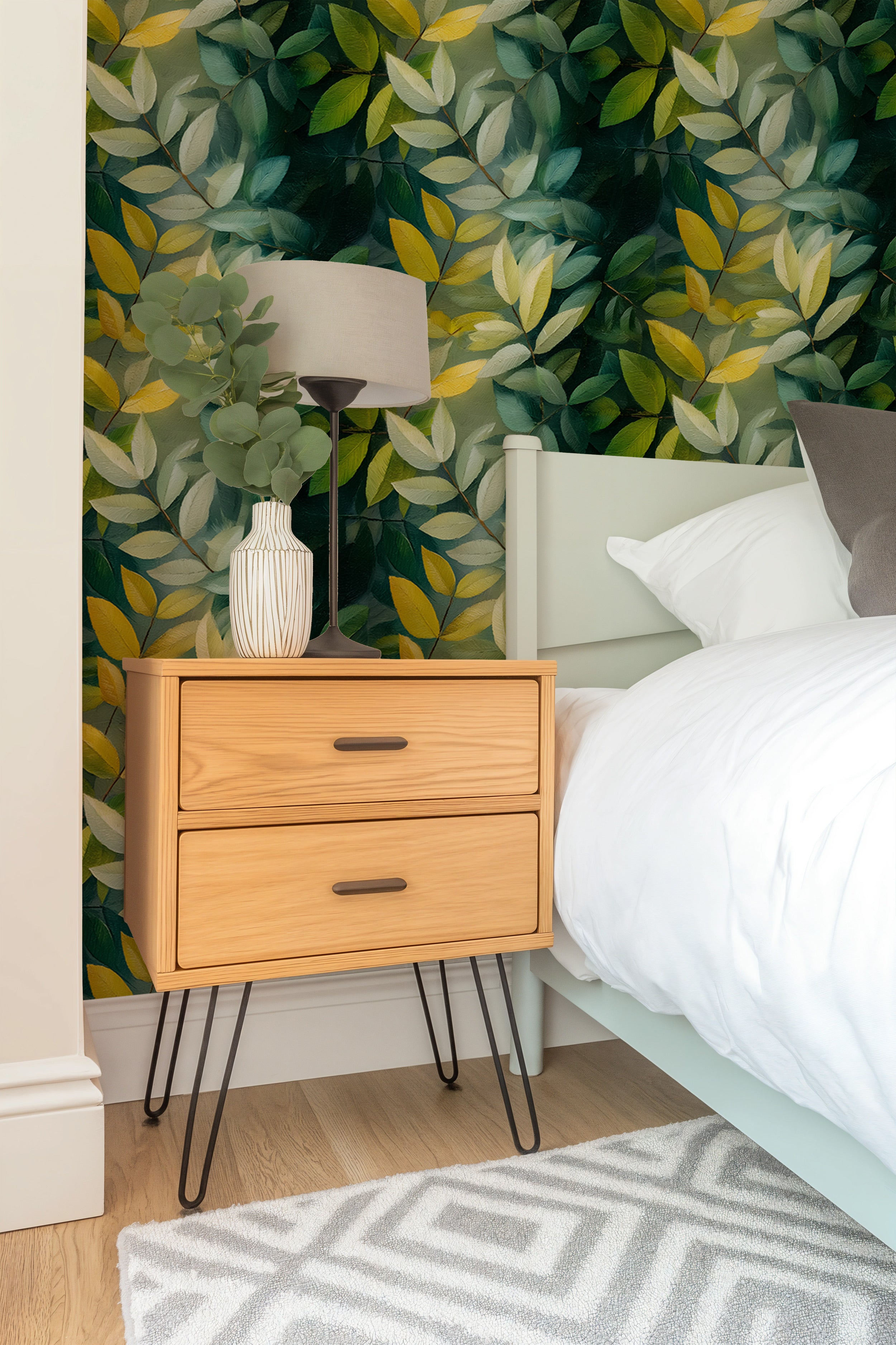 Green tropical leaf wallpaper in a bedroom setting with a light wood nightstand and white linens, lush emerald and yellow fol