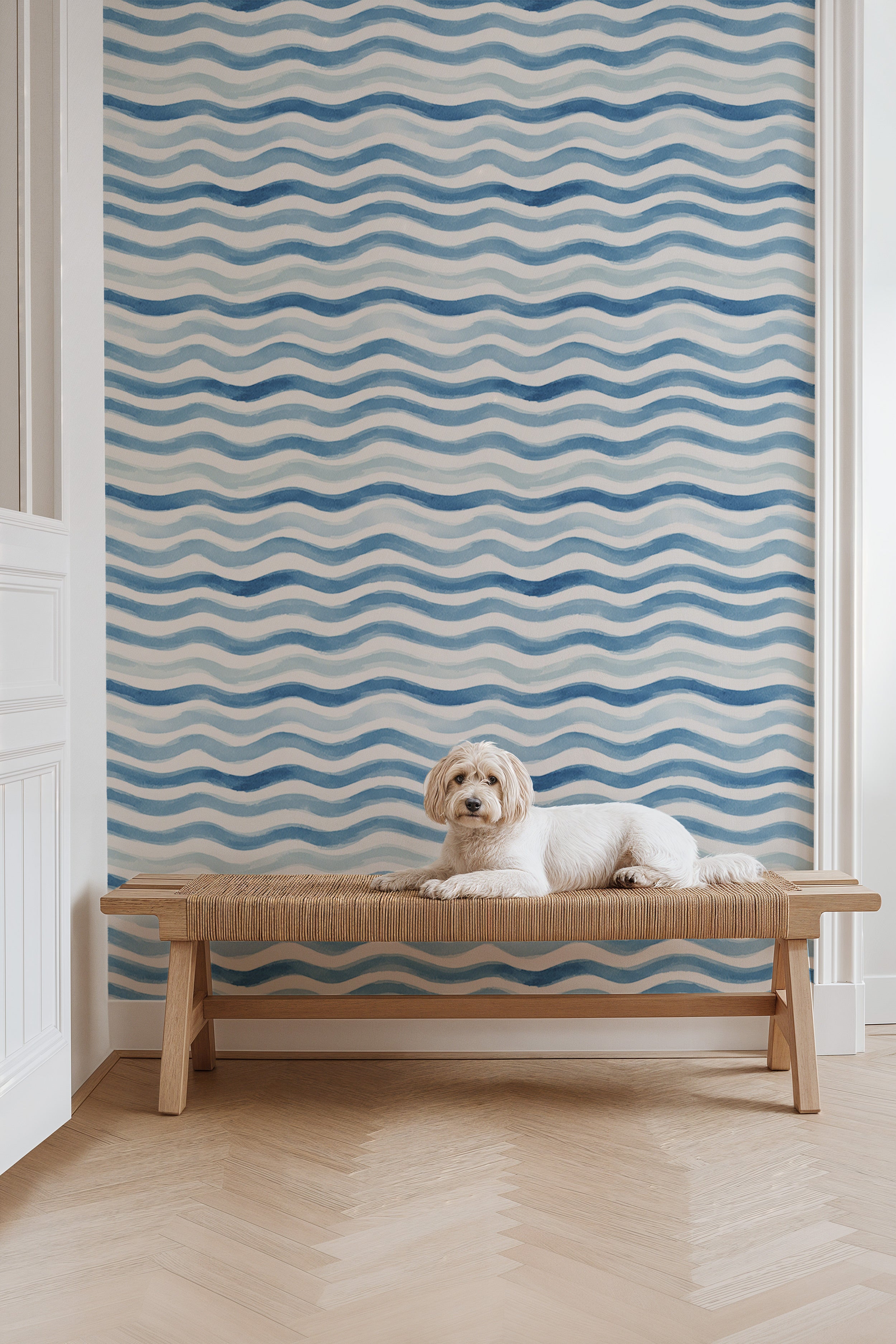 White dog lounging on a wooden bench against blue watercolor wave pattern wallpaper in a bright coastal-inspired room
